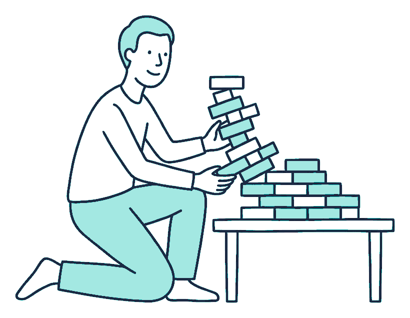 A person kneels at a low table rearranging a toppled tower of blocks into a neater, wider stack